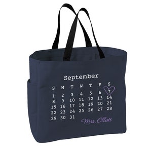 May include: A navy blue tote bag with black handles and a side pocket. The bag displays a September calendar, highlighting the 7th with a purple heart. The name "Mrs. Elliott" is written below the calendar.