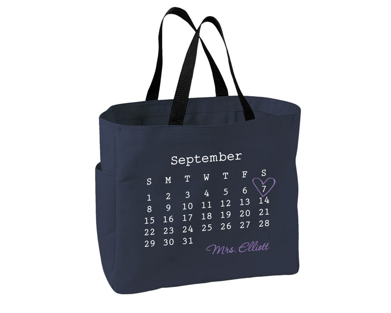 May include: A navy blue tote bag with black handles and a side pocket. The bag displays a September calendar, highlighting the 7th with a purple heart. The name "Mrs. Elliott" is written below the calendar.