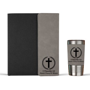 May include: A gray faux leather journal with a black cover and a matching gray faux leather tumbler. Both items feature a black cross with a laurel wreath and the text "2 Timothy 4:2 Pastor Tracy W. Wilson".