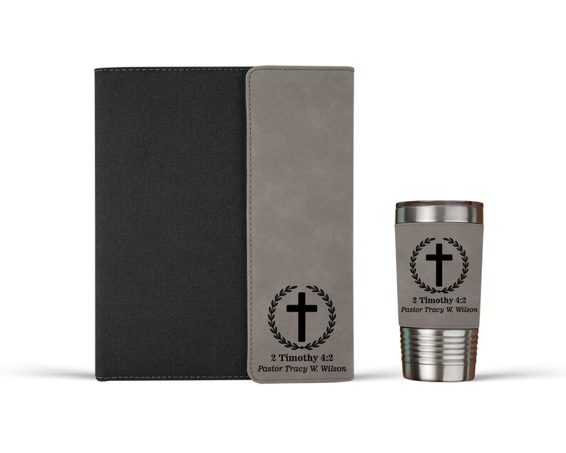 May include: A gray faux leather journal with a black cover and a matching gray faux leather tumbler. Both items feature a black cross with a laurel wreath and the text "2 Timothy 4:2 Pastor Tracy W. Wilson".