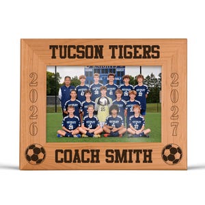 May include: Wooden picture frame with the text "TUCSON TIGERS" and "COACH SMITH". The frame holds a team photo of a soccer team. The frame has soccer ball and year 2026 and 2027 designs.
