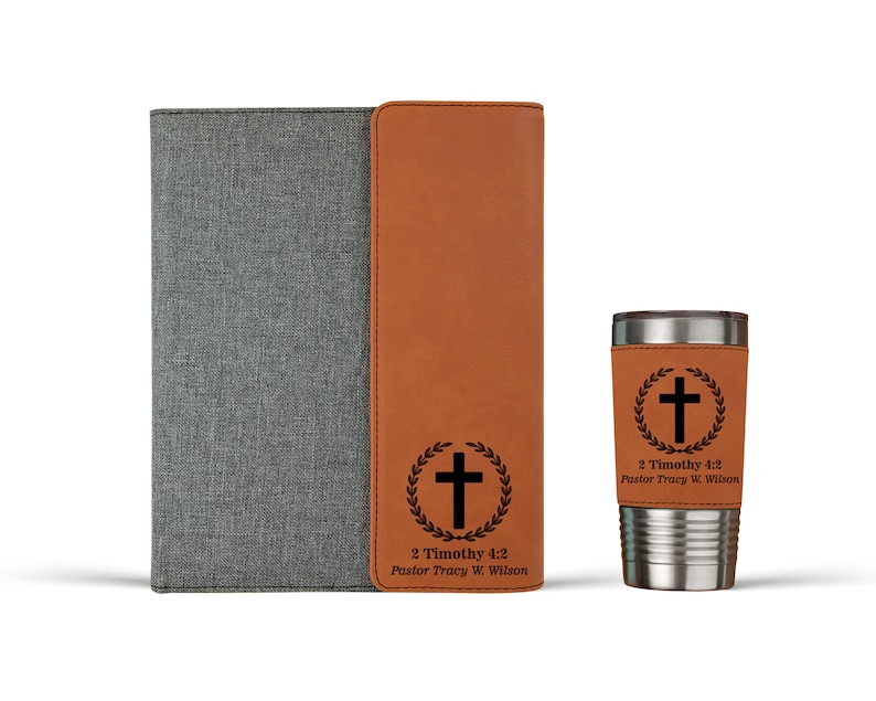 May include: A brown leatherette journal with a gray fabric cover and a matching brown leatherette tumbler. Both items feature a black cross with a laurel wreath and the text "2 Timothy 4:2 Pastor Tracy W. Wilson".