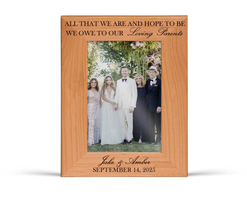 May include: A rectangular light brown wooden picture frame featuring the engraved text ALL THAT WE ARE AND HOPE TO BE WE OWE TO OUR Loving Parents at the top and Jake & Amber SEPTEMBER 14, 2025 at the bottom, holding a wedding photograph.