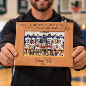 May include: A rectangular light brown wooden picture frame featuring the engraved text A GOOD COACH CAN CHANGE A GAME A GREAT COACH CAN CHANGE A Life at the top and Coach Wes 2026 at the bottom, containing a photo of a basketball team.