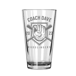 May include: A clear glass pint glass featuring a gray etched design of a baseball glove and two crossed bats inside a shield. The text reads COACH DAVE at the top, MUDSLINGERS at the bottom, and the numbers 20 and 22 on the left and right sides.