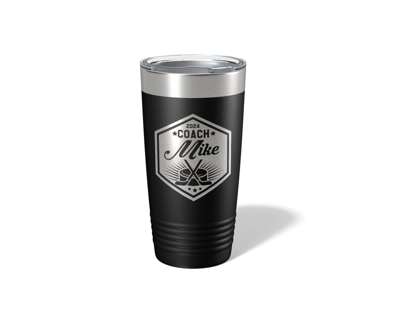 May include: A black stainless steel tumbler with a clear lid. The front features a silver laser-engraved hexagonal emblem containing the text 2024 COACH Mike, with a graphic of two crossed hockey sticks and a puck centered below the name.