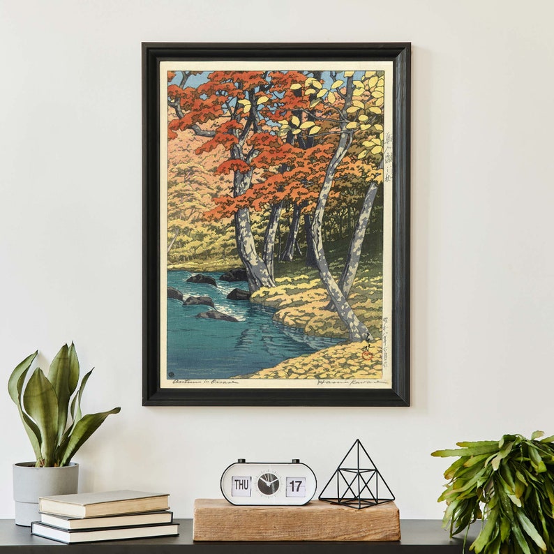 May include: A framed woodblock print of a Japanese landscape with a river flowing through a forest of trees with red, yellow, and green leaves. The print is titled "Autumn in Kiso".