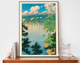 May include: A vintage Japanese woodblock print depicting a serene lakeside scene. Lush green trees frame a tranquil body of water reflecting the blue sky and fluffy white clouds. The print features a traditional Japanese aesthetic with vibrant colors and delicate details.