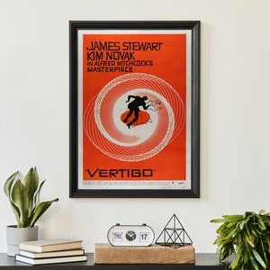 May include: A framed movie poster for the film "Vertigo" starring James Stewart and Kim Novak. The poster features a red and white spiral design with a silhouette of a man running in the center. The text on the poster reads "James Stewart Kim Novak in Alfred Hitchcock's Masterpiece Vertigo".