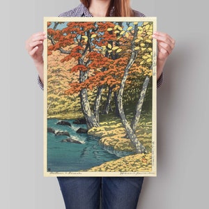 May include: A woodblock print depicting a Japanese landscape with a river flowing through a forest of trees with red, orange, and yellow leaves. The print is titled "Autumn in Japan" and signed by the artist, "Hiroshige".