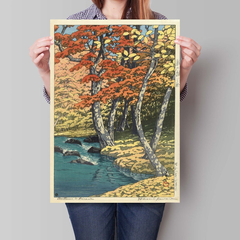 May include: A woodblock print depicting a Japanese landscape with a river flowing through a forest of trees with red, orange, and yellow leaves. The print is titled "Autumn in Japan" and signed by the artist, "Hiroshige".