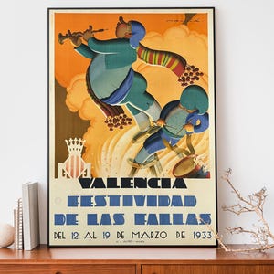 May include: A framed vintage poster advertising the Valencia Fallas Festival in Spain, 1933. The artwork features two figures in blue and green clothing, one playing a wind instrument. The poster has text in Spanish and is set against an orange and yellow background.