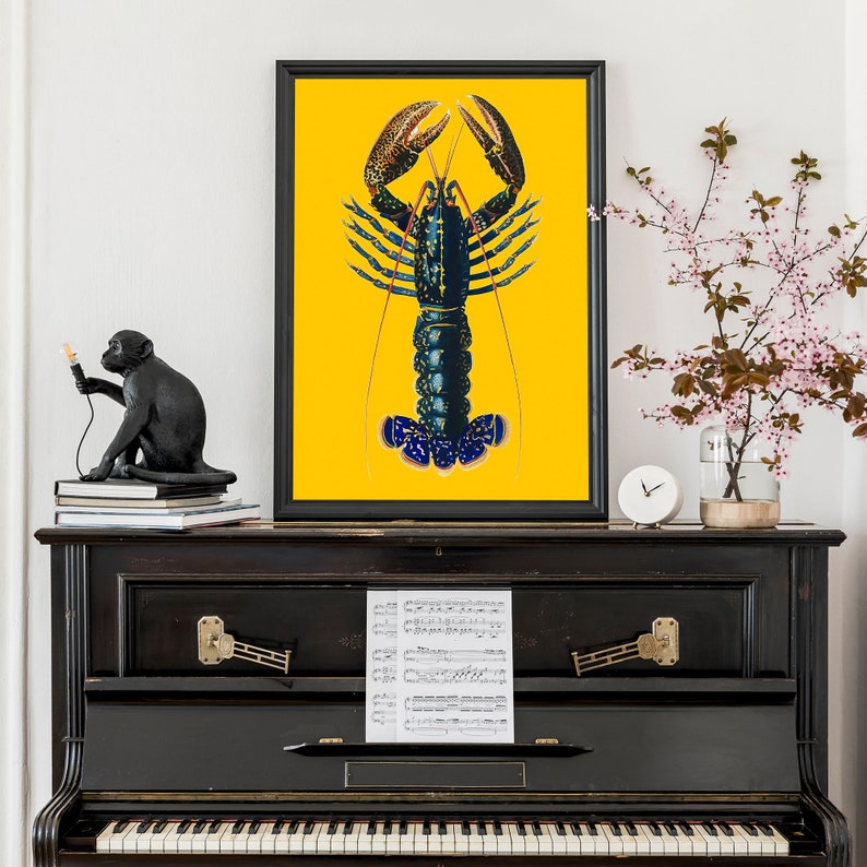 Puede incluir: Una ilustraci&oacute;n vintage de una langosta azul sobre un fondo amarillo. La langosta est&aacute; representada en un estilo realista y detallado, con las garras levantadas. La imagen est&aacute; enmarcada y se muestra en un piano negro.