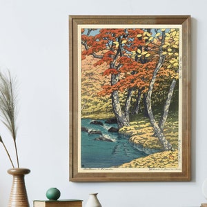 May include: A framed woodblock print of a Japanese landscape scene with a river flowing through a forest of trees with red, orange, and yellow leaves. The print is titled "Autumn in Japan" and signed by the artist, "Hiroshi Yoshida."