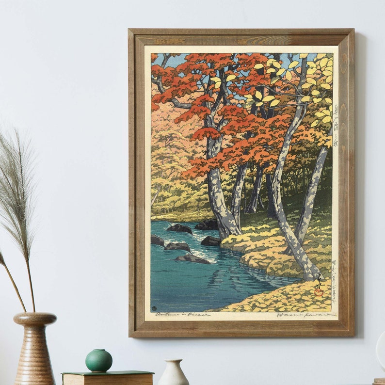 May include: A framed woodblock print of a Japanese landscape scene with a river flowing through a forest of trees with red, orange, and yellow leaves. The print is titled "Autumn in Japan" and signed by the artist, "Hiroshi Yoshida."