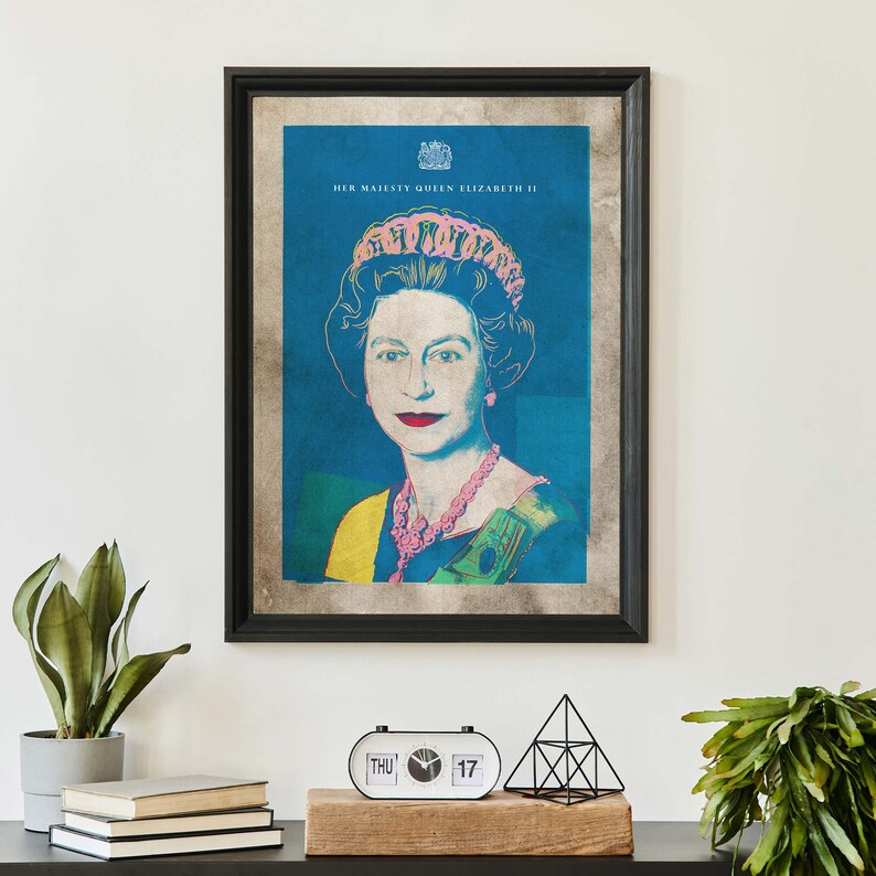 May include: A framed print of Queen Elizabeth II in a pop art style. The background is blue, and the queen is wearing a pink crown and a yellow and green necklace. The text "HER MAJESTY QUEEN ELIZABETH II" is at the top of the print.