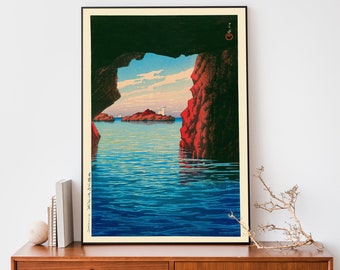 May include: A Japanese woodblock print depicting a seascape view from a cave. The water is a deep blue with ripples and reflections of the sky. The cave walls are dark green and red. The sky is a light blue with white clouds. There are small white boats in the distance.