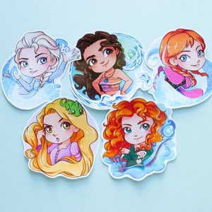 以下が含まれることがあります： アニメの女性キャラクターが描かれた5つの漫画ステッカーのコレクション。各ステッカーは、ユニークな髪型と衣装の異なるキャラクターを、水色の背景に表示しています。ステッカーには、エルサ、モアナ、アナ、ラプンツェル、メリダが含まれています。