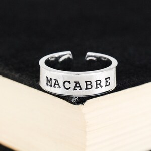 May include: A silver ring with the word "MACABRE" engraved in black lettering.