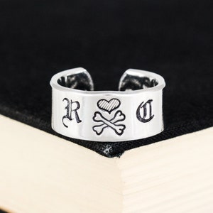 Könnte beinhalten: Silberring mit einem Herz- und Totenkopfdesign und den Buchstaben "R" und "C" auf beiden Seiten.