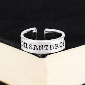 May include: A silver ring with the word "MISANTHROP" engraved on it.