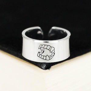 May include: A silver ring with a graphic of a set of fangs. The ring is a simple band with a flat top.