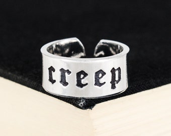May include: A silver adjustable ring with the word "creep" written in black gothic lettering.