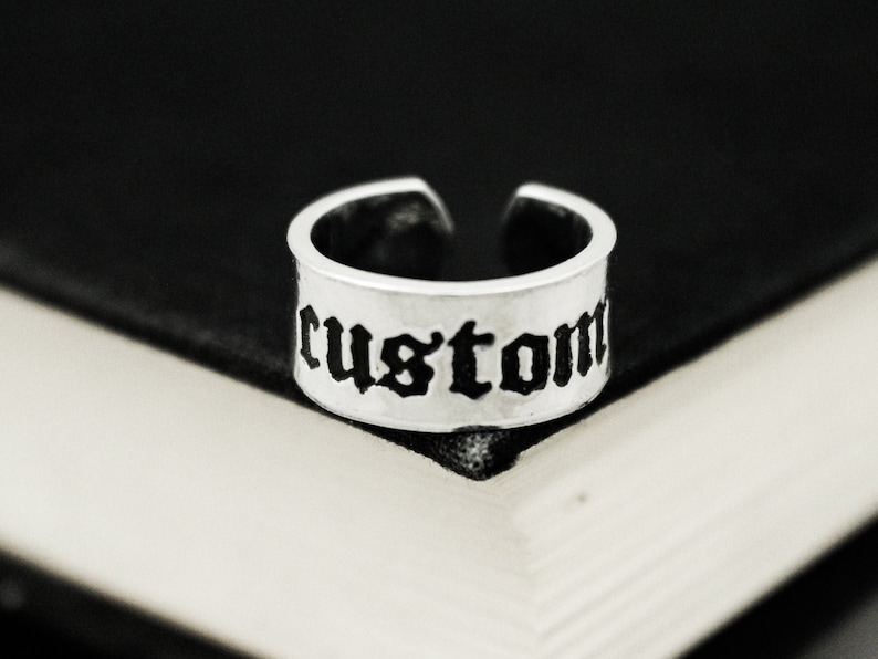 May include: A silver ring with the word "custom" engraved in black gothic lettering.