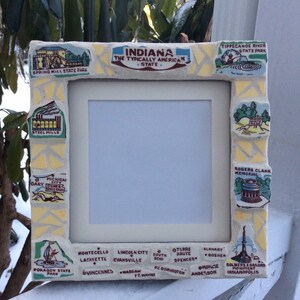 May include: A yellow and white mosaic picture frame with a white mat and a clear glass insert. The frame is decorated with images of Indiana landmarks and locations, including Spring Mill State Park, Steel Mills, Michigan City, Gary Dunes State Park, Pokagon State Park, Tippecanoe River State Park, Rogers Clark Memorial, Montecello, Lafayette, Lincoln City, Evansville, South Bend, Terre Haute, Spencer, Elkhart, Goshen, Vincennes, Warsaw, Fort Wayne, Bloomington, Anderson, Muncie, and Soldiers & Sailors Monument Indianapolis.