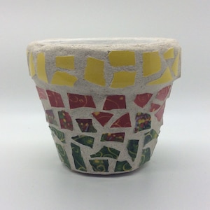 May include: A small, round, concrete planter with a mosaic design. The mosaic is made of small, colorful tiles in shades of yellow, red, and green.