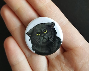 May include: A black cat with yellow eyes is featured on a white button.