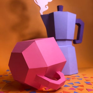 May include: A pink papercraft model of a teapot with a handle, sitting on a table with orange, pink, and blue confetti. A purple papercraft model of a coffee pot with a white papercraft model of steam rising from the spout is behind the teapot.