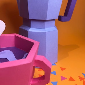 May include: A pink paper coffee cup with a purple interior and a purple swirl design. The cup is next to a purple and blue paper coffee pot on a bright orange background with scattered blue, pink, and orange paper triangles.