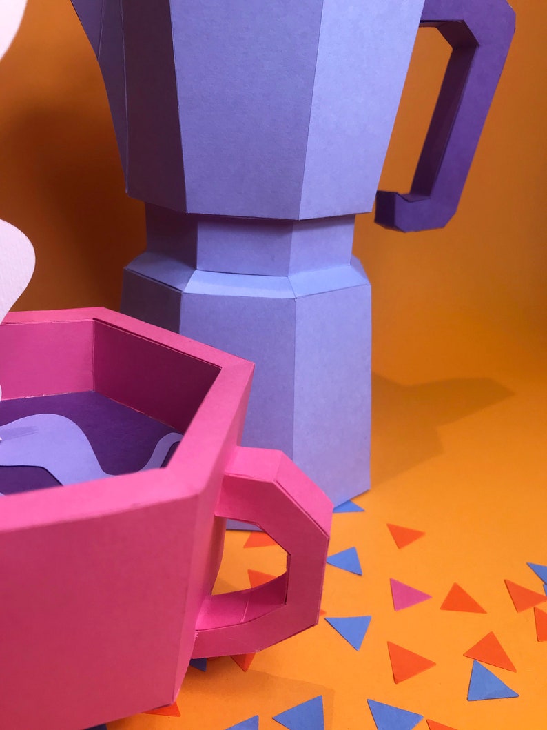 May include: A pink paper coffee cup with a purple interior and a purple swirl design. The cup is next to a purple and blue paper coffee pot on a bright orange background with scattered blue, pink, and orange paper triangles.