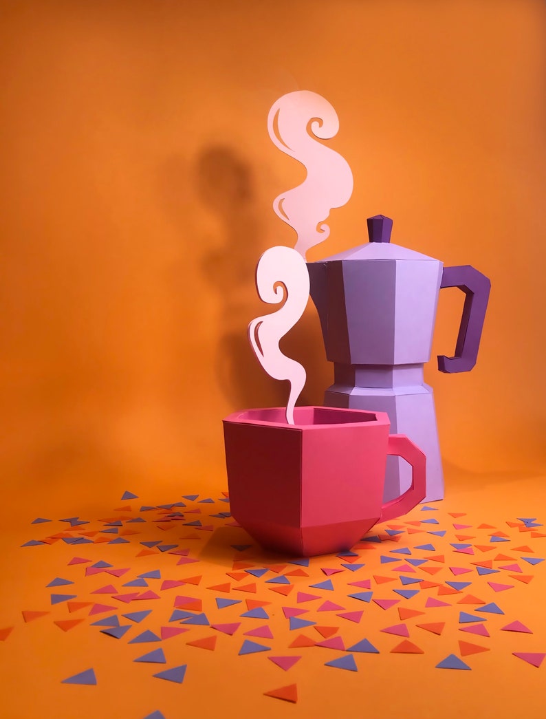 May include: A purple paper coffee pot with a pink paper coffee cup and white paper steam rising from the cup. The coffee pot and cup are sitting on an orange surface with scattered blue, pink, and orange paper triangles.