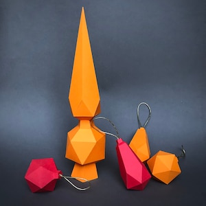May include: Five geometric paper ornaments in orange and red. The ornaments are in the shape of a star, a teardrop, and three round shapes. The ornaments are hanging from a string.