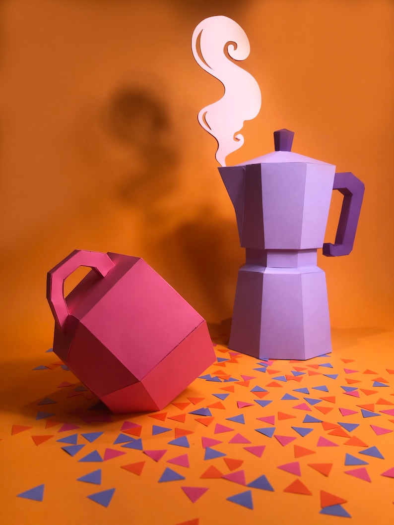 May include: A purple paper coffee pot with a white paper steam design above it. A pink paper container with a handle is on the left side of the image. The objects are on an orange surface with scattered blue, pink, and orange paper triangles.
