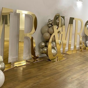 May include: Gold mirrored letters spelling "MR & MRS" with balloon decorations in beige and white.