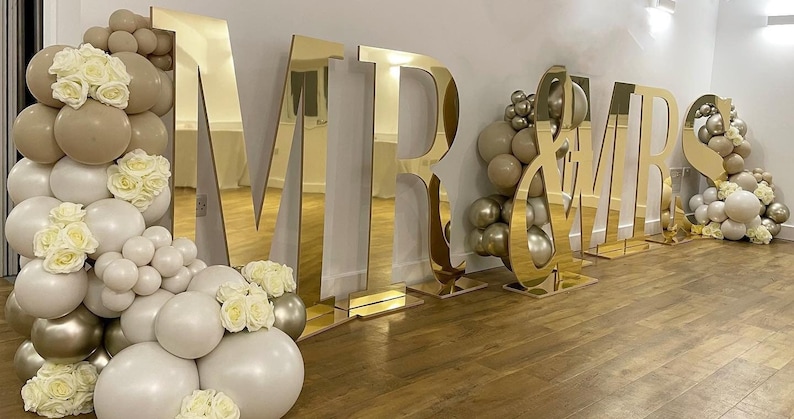 May include: Gold mirrored letters spelling "MR & MRS" with balloon decorations in beige and white.