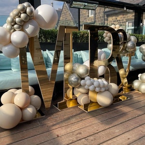 May include: Gold letters spelling "MR & MRS" decorated with white, gold, and champagne colored balloons.
