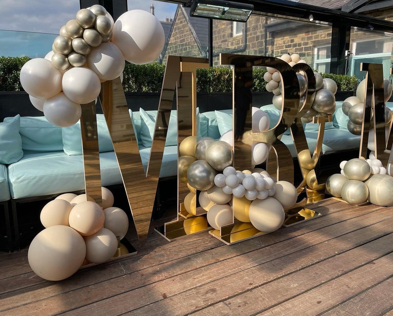 May include: Gold letters spelling "MR & MRS" decorated with white, gold, and champagne colored balloons.