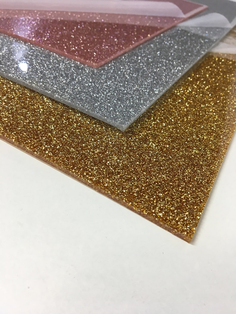 Puede incluir: Tres hojas de papel de purpurina en dorado, plateado y rosa dorado. Las hojas est&aacute;n apiladas una encima de la otra.