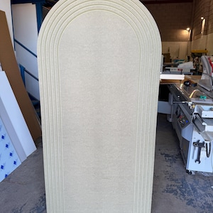 May include: An off-white arched panel, featuring a series of curved, recessed lines. The panel has a rectangular base and a rounded top, with the lines echoing the arch. The material appears to be a composite wood product, suitable for interior design.