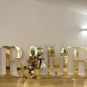 May include: Gold mirrored letters spelling "MR & MRS" with white and beige balloons on either side.