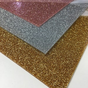 Puede incluir: Tres hojas de papel de purpurina en dorado, plateado y rosa dorado. Las hojas est&aacute;n apiladas una encima de la otra.