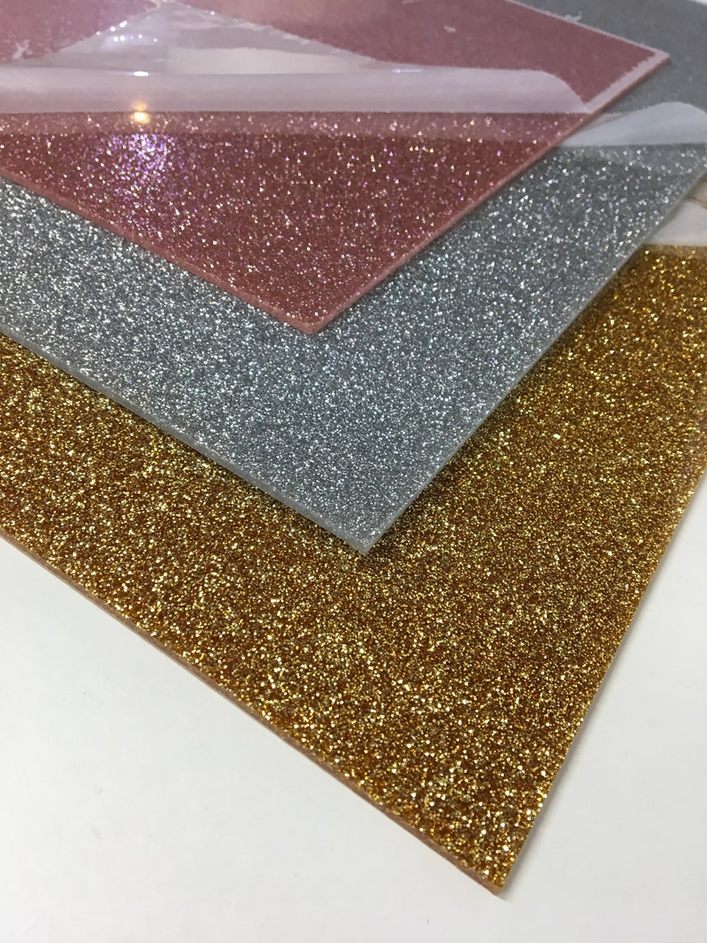 Puede incluir: Tres hojas de papel de purpurina en dorado, plateado y rosa dorado. Las hojas est&aacute;n apiladas una encima de la otra.