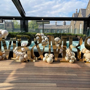 May include: Gold "Mr & Mrs" letters with white and beige balloons on a wooden floor.