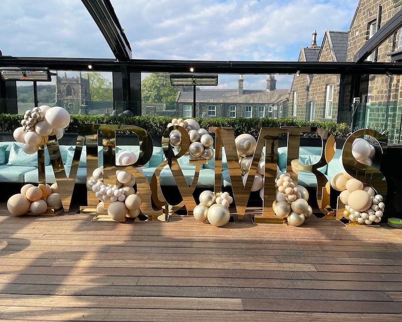 May include: Gold "Mr & Mrs" letters with white and beige balloons on a wooden floor.
