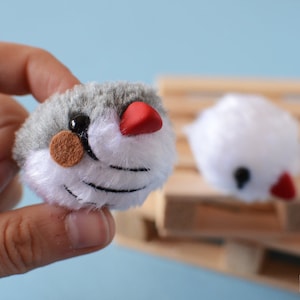 Pode incluir: Dois pequenos brinquedos de pássaros de pelúcia. Um é cinza com a barriga branca e o bico vermelho. O outro é branco com o bico vermelho. Ambos têm olhos pretos.