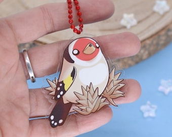 May include: A clear acrylic charm featuring a cartoon goldfinch bird with a red face, white cheeks, and a yellow wing. The charm is attached to a red beaded chain. The text "PICK CHICK" is in the upper left corner.